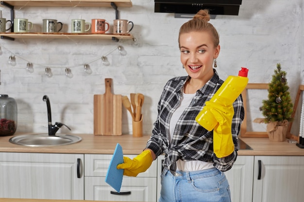 Giovane donna professionale che indossa guanti gialli protettivi in gomma che tengono detergenti per bottiglie in cucina.