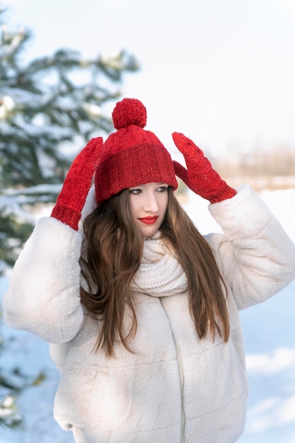 Giovane donna raddrizza cappello in winter park su sfondo parco innevato Telaio verticale Giornata invernale di sole