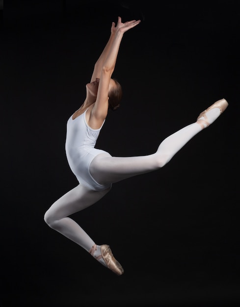 Giovane donna relativa alla ginnastica che salta nel corpo bianco isolato su fondo nero