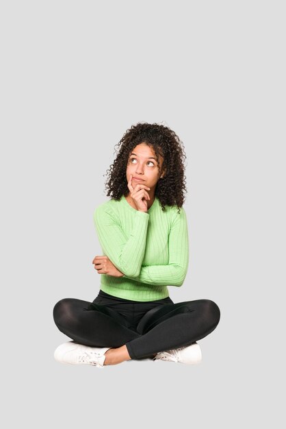 Giovane donna riccia afroamericana che si siede sul pavimento isolato