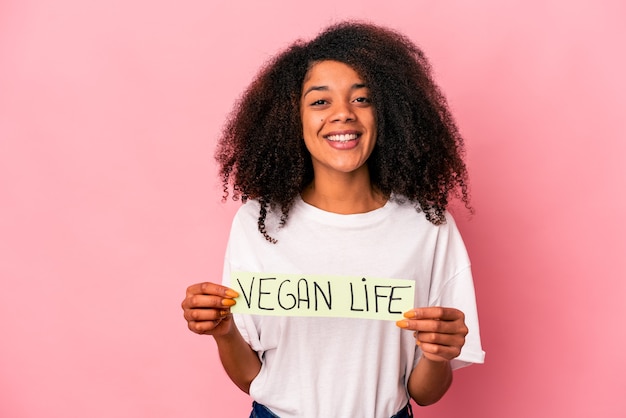 Giovane donna riccia afroamericana che tiene un cartello di vita vegano felice, sorridente e allegro.