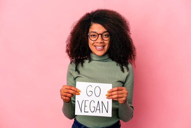 Giovane donna riccia afroamericana che tiene un cartello vegano felice, sorridente e allegro.