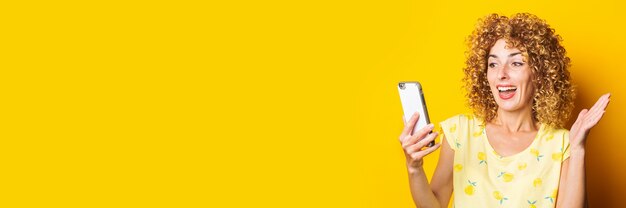 Giovane donna riccia che chiacchiera dal telefono su una superficie gialla