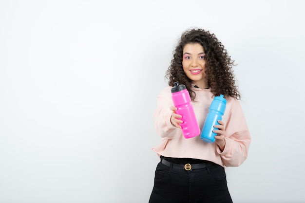 Giovane donna riccia in maglione che tiene bottiglie d'acqua rosa e blu.