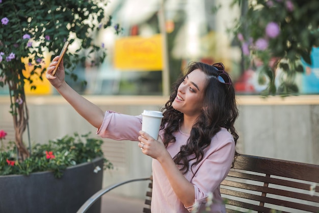 Giovane donna riccia usa un telefono per i social network Una modella si fa un selfie per strada in una città europea in estate Videochiamata