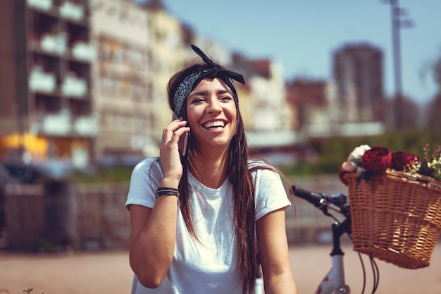 Giovane donna ridente che parla sullo smartphone in una giornata di sole, accanto alla bici con cesto di fiori.