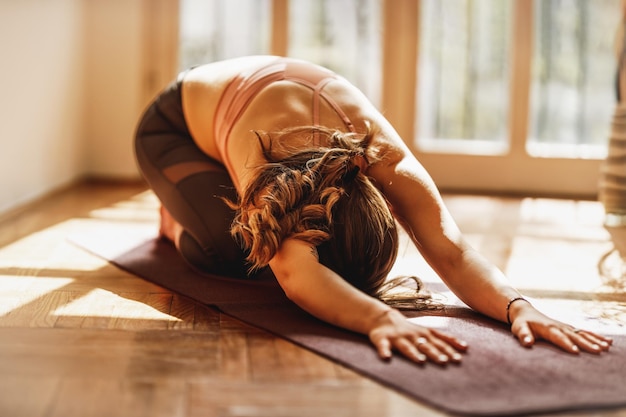 Giovane donna rilassata che pratica yoga nella posa del bambino a casa.