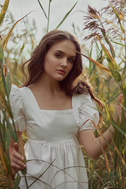 Giovane donna romantica in erba alta e spessa in campo Donna gentile sognante in un abito bianco in natura Bellezza naturale godimento della vita