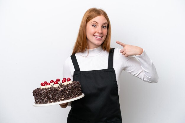 Giovane donna rossa che tiene torta di compleanno isolata su sfondo bianco dando un pollice in alto gesto