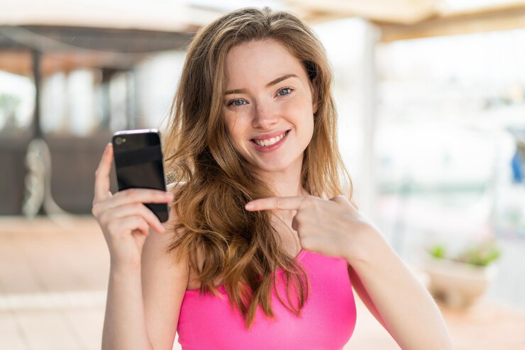 Foto giovane donna rossa che usa il cellulare all'aperto e lo punta