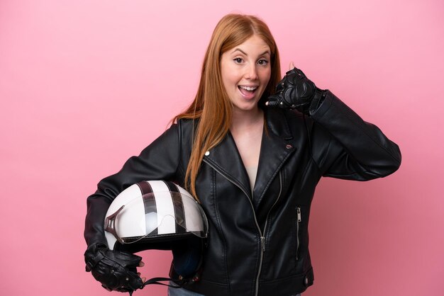 Giovane donna rossa con un casco da motociclista isolato su sfondo rosa che fa il gesto del telefono Chiamami indietro segno