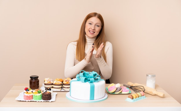 Giovane donna rossa con una grande torta applaudire