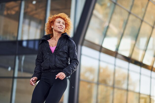 Giovane donna rossa europea in abiti sportivi facendo fitness all'aperto