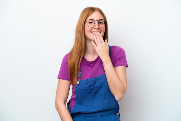 Giovane donna rossa isolata su sfondo bianco felice e sorridente che copre la bocca con la mano