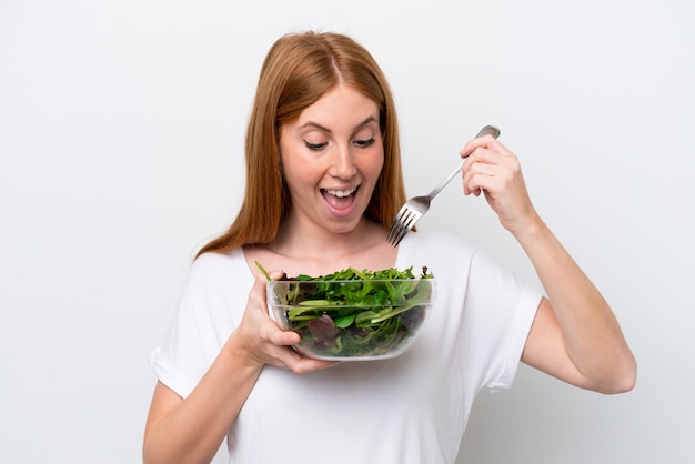 Giovane donna rossa isolata su sfondo bianco in possesso di una ciotola di insalata con felice espressione