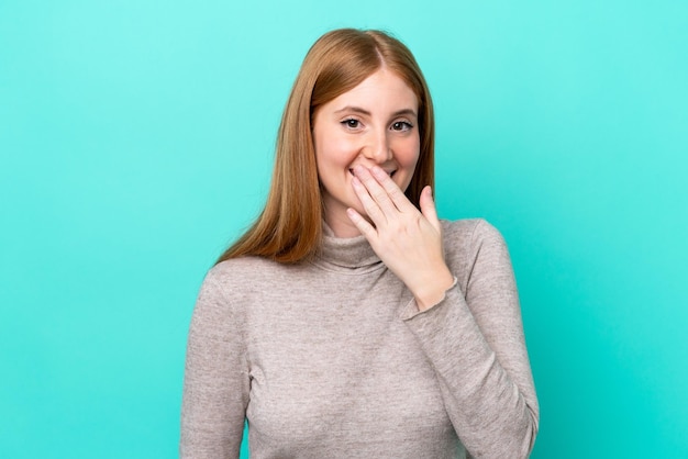 Giovane donna rossa isolata su sfondo blu felice e sorridente che copre la bocca con la mano