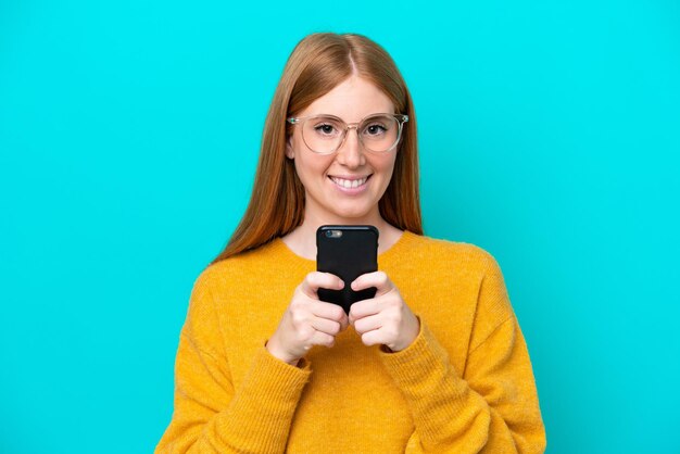 Giovane donna rossa isolata su sfondo blu guardando la telecamera e sorridente