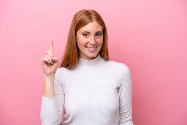 Giovane donna rossa isolata su sfondo rosa che indica una grande idea