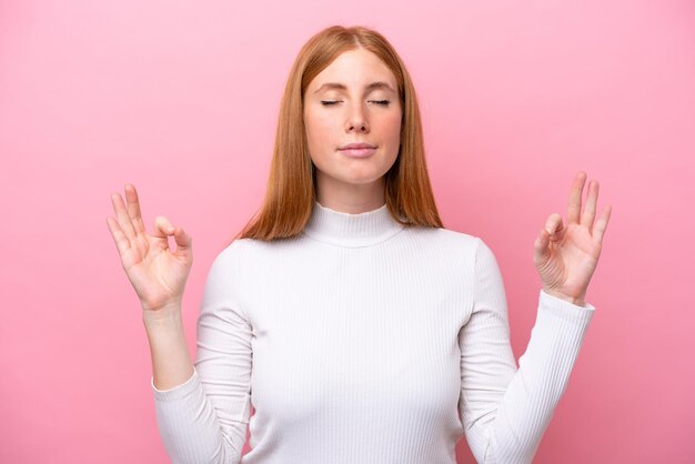 Giovane donna rossa isolata su sfondo rosa in posa zen