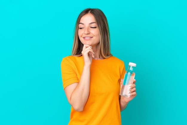 Giovane donna rumena con una bottiglia d'acqua isolata su sfondo blu guardando di lato e sorridente