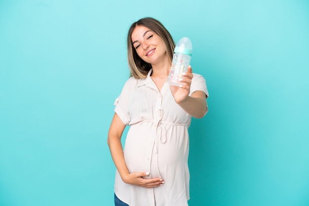 Giovane donna rumena isolata su sfondo blu incinta e in possesso di un biberon