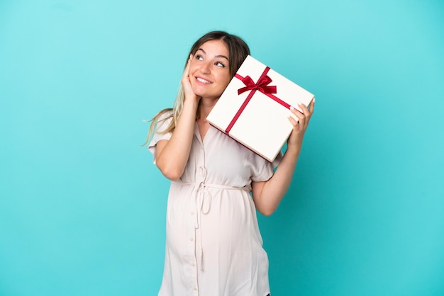Giovane donna rumena isolata su sfondo blu incinta e in possesso di un regalo