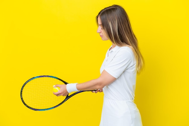 Giovane donna rumena isolata su sfondo giallo giocando a tennis