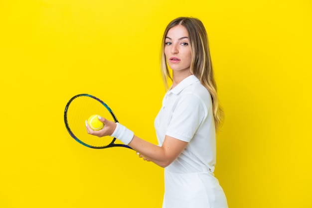 Giovane donna rumena isolata su sfondo giallo giocando a tennis