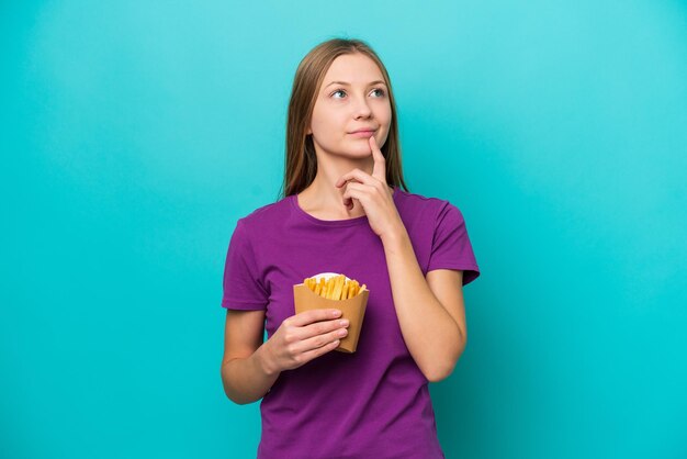 Giovane donna russa che cattura patatine fritte isolate su sfondo blu che ha dubbi mentre guarda in alto