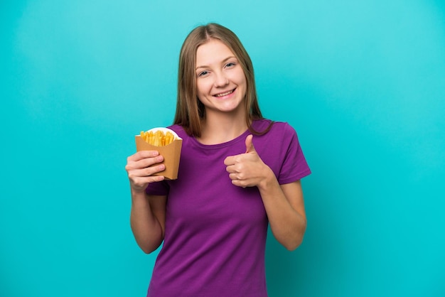 Giovane donna russa che cattura patatine fritte isolate su sfondo blu dando un pollice in alto gesto