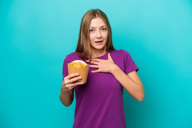 Giovane donna russa che cattura patatine fritte isolate su sfondo blu sorpreso e scioccato mentre guarda a destra