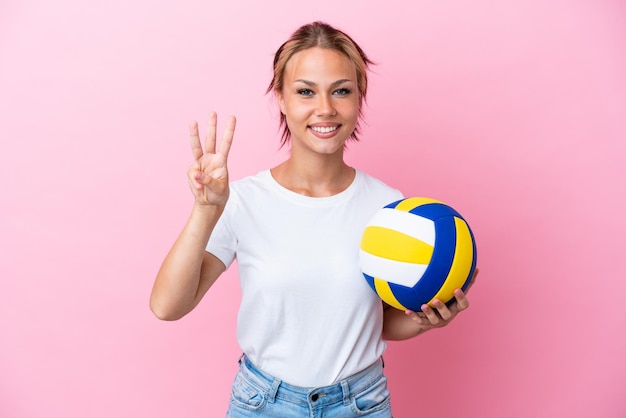 Giovane donna russa che gioca a pallavolo isolata su sfondo rosa felice e contando tre con le dita