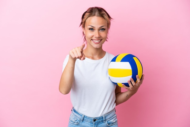 Giovane donna russa che gioca a pallavolo isolata su sfondo rosa sorpresa e puntata davanti