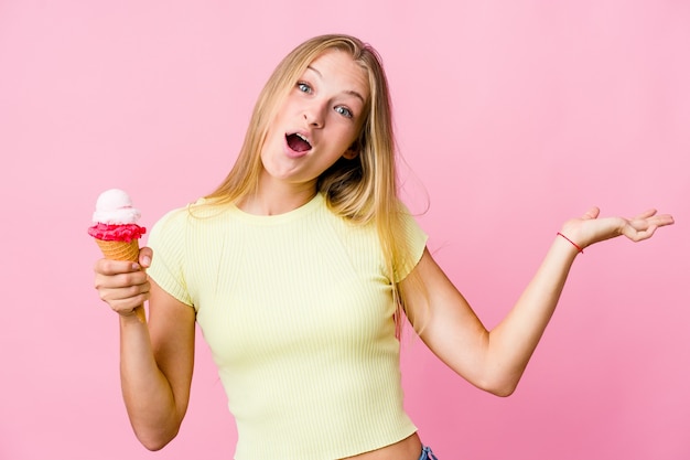 Giovane donna russa che mangia un gelato isolato celebrando una vittoria o un successo, è sorpreso e scioccato.
