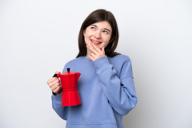 Giovane donna russa che tiene caffettiera isolata su sfondo bianco alzando lo sguardo mentre sorride