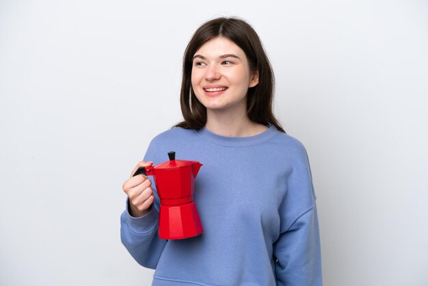 Giovane donna russa che tiene caffettiera isolata su sfondo bianco guardando al lato e sorridente