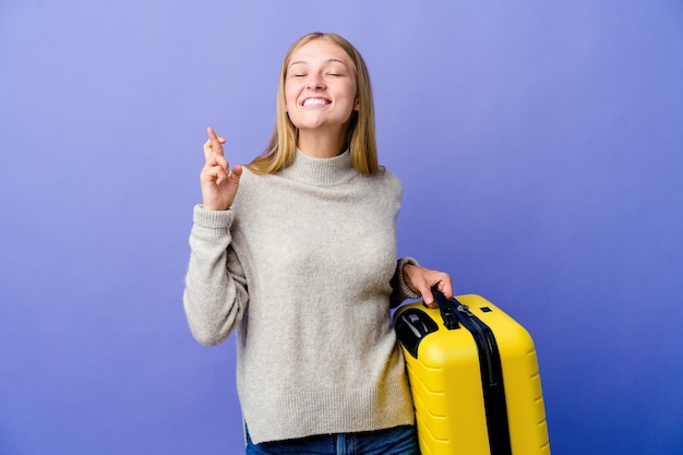 Giovane donna russa che tiene la valigia per viaggiare incrociando le dita per avere fortuna