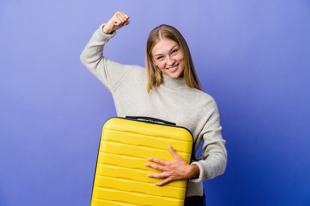 Giovane donna russa che tiene la valigia per viaggiare mostrando il gesto di forza con le braccia, simbolo del potere femminile