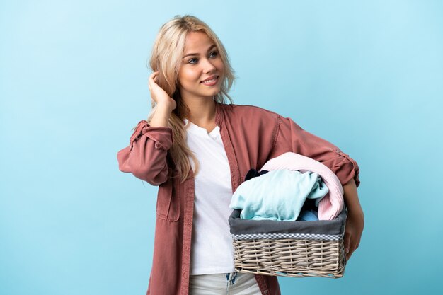 Giovane donna russa che tiene un cestino dei vestiti isolato sulla parete blu che pensa un'idea