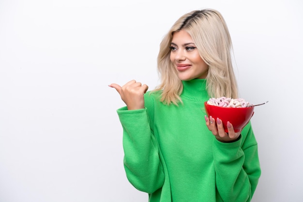 Giovane donna russa che tiene una ciotola di cereali isolata su sfondo bianco che indica il lato per presentare un prodotto