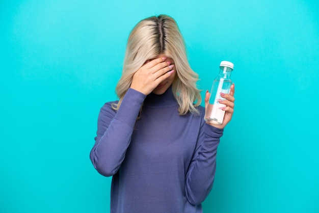 Giovane donna russa con una bottiglia d'acqua isolata su sfondo blu con espressione stanca e malata