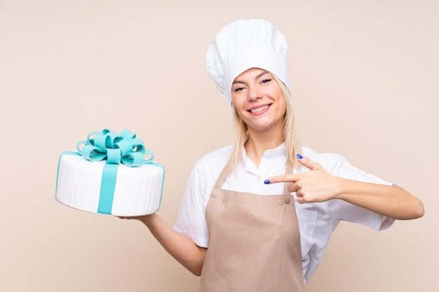 Giovane donna russa con una grande torta sul muro isolato e puntandolo