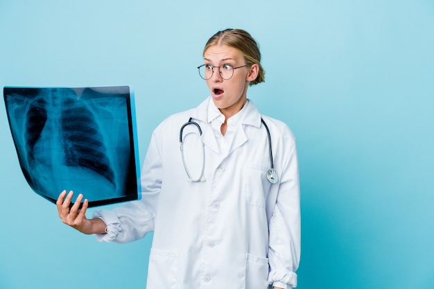Giovane donna russa del medico che tiene una scintigrafia ossea sul blu che è scioccata a causa di qualcosa che ha visto.