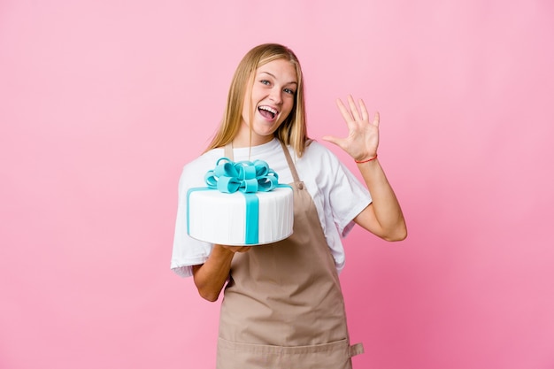 Giovane donna russa del panettiere che tiene una torta deliziosa che mostra il numero dieci con le mani.