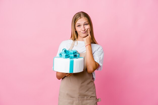 Giovane donna russa del panettiere che tiene una torta deliziosa dubitando tra due opzioni.