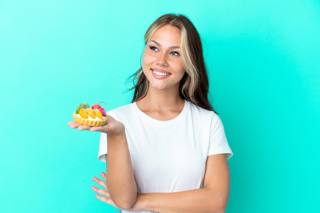 Giovane donna russa in possesso di un dolce di frutta isolato su sfondo blu guardando il lato