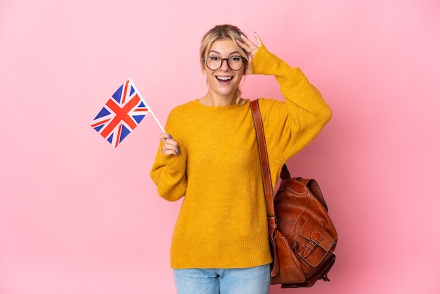 Giovane donna russa in possesso di una bandiera del Regno Unito isolata su sfondo rosa con espressione di sorpresa