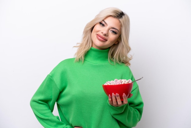 Giovane donna russa in possesso di una ciotola di cereali isolata su sfondo bianco in posa con le braccia all'anca e sorridente
