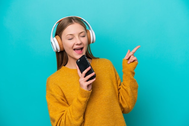 Giovane donna russa isolata su sfondo blu ascoltando musica con un cellulare e cantando