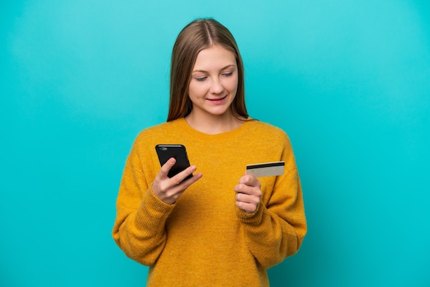 Giovane donna russa isolata su sfondo blu che acquista con il cellulare con una carta di credito